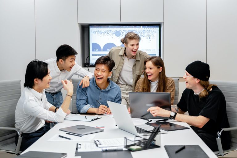 a group of people sitting around a table with laptops