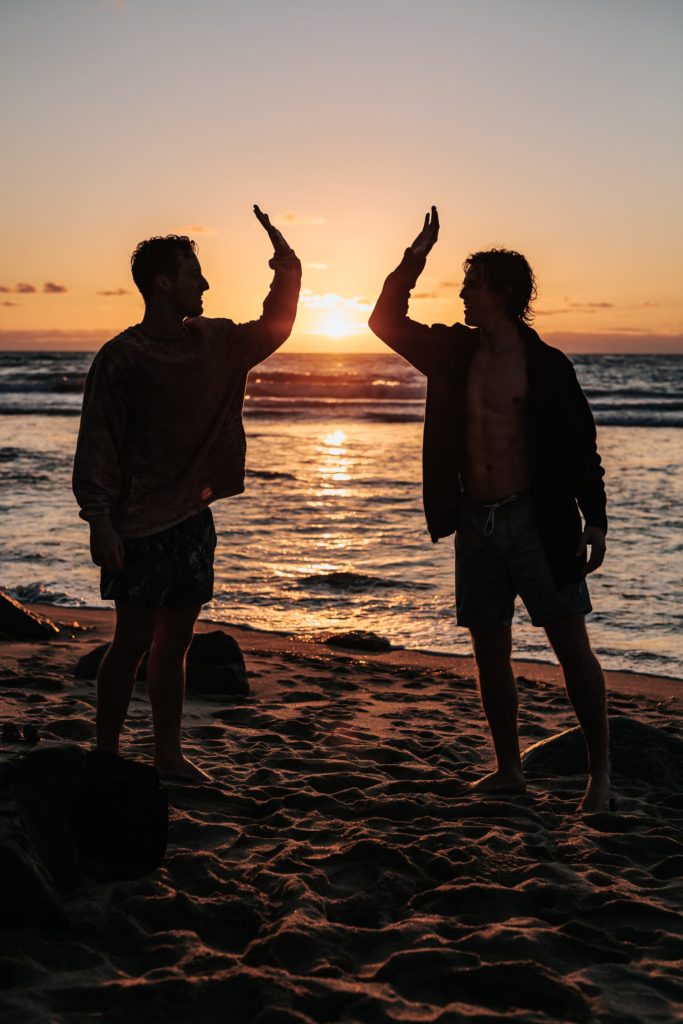 a man and woman standing on a beach with their arms raised