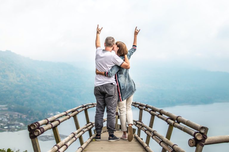 a man and woman standing on a wooden bridge with their arms up