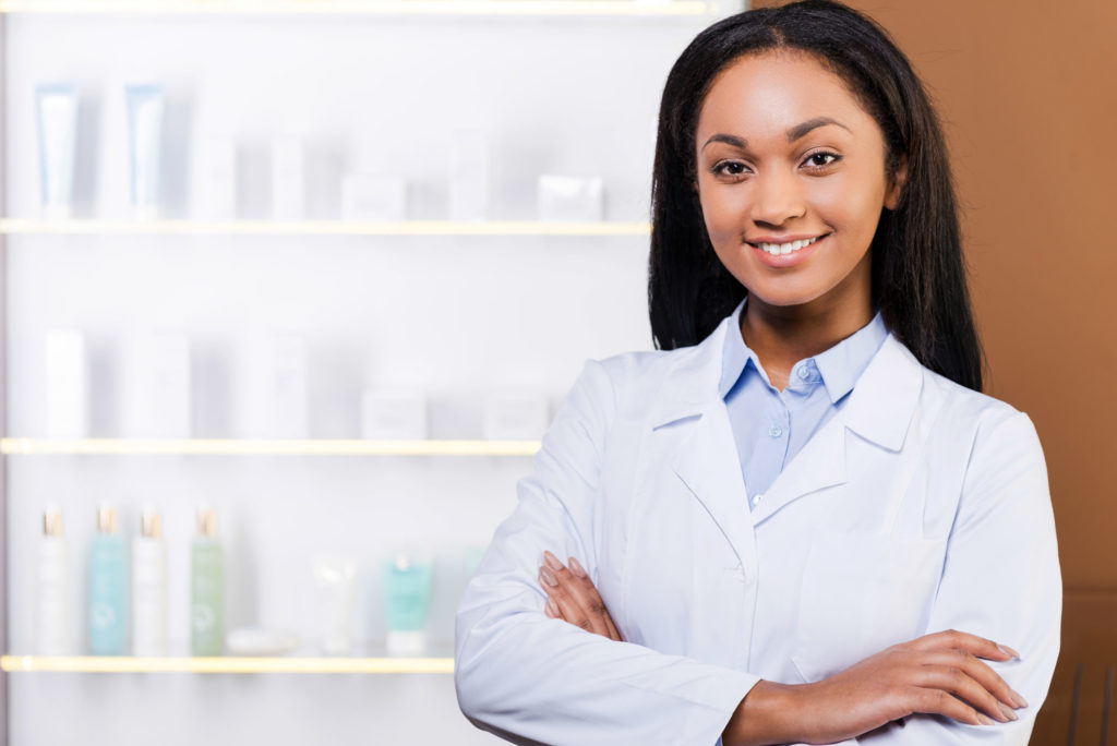 a person smiling in front of a shelf of medicine