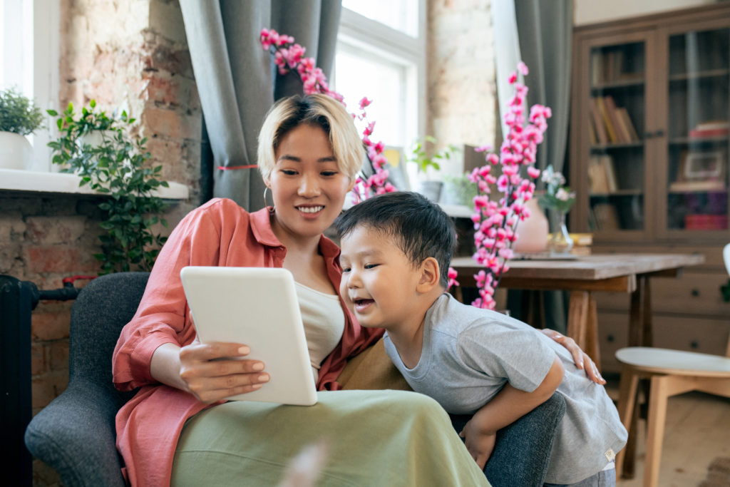 Happy young mother and her cute little son watching online video