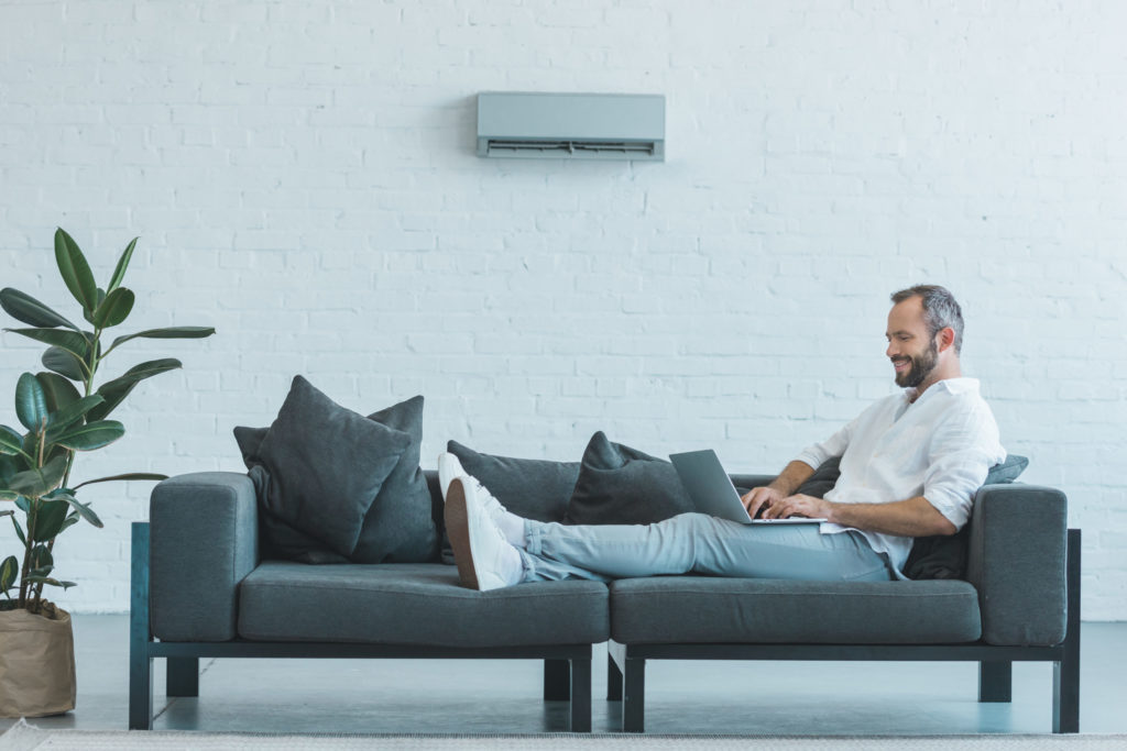 handsome man working with laptop on sofa, with air conditioner on wall at home